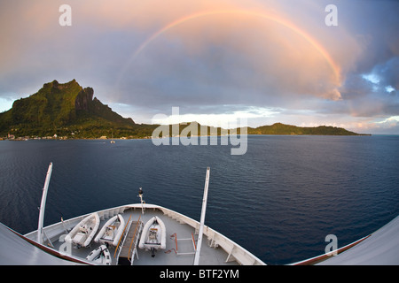 Visto da una nave, un tardo pomeriggio rainbow passa sopra l'isola vulcanica di Bora Bora. Polinesia francese, Oceano Pacifico. Foto Stock