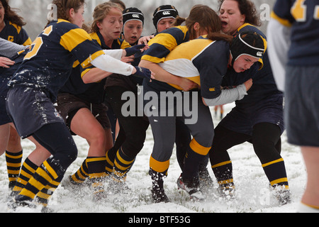 Un accademia navale sfera portante è affrontato da George Washington University giocatori durante un snowy donna partita di rugby. Foto Stock