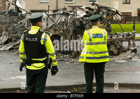 Due ufficiali della polizia sulla scena di disordini civili, dove un autobus è stato dirottato e bruciato. Foto Stock