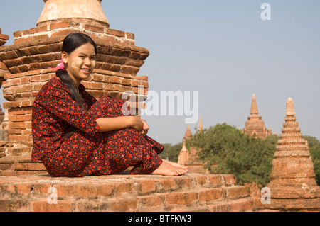 Giovane donna birmano in un abito rosso seduta sul tetto di un tempio , Bagan (pagano), Myanmar (Birmania) Foto Stock