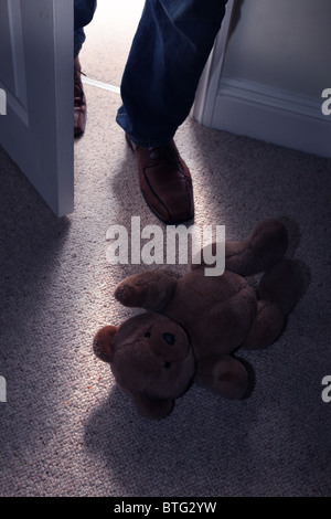 Per bambini orsacchiotto giacente sul piano di un pavimento in moquette come un uomo i piedi di passo in una porta aperta Foto Stock