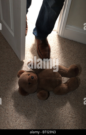 Per bambini orsacchiotto giacente sul piano di un pavimento in moquette come un uomo di piedi in fase attraverso una porta aperta Foto Stock