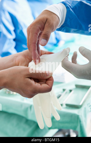 Personale medico di mettere le mani sui guanti in sala operatoria Foto Stock