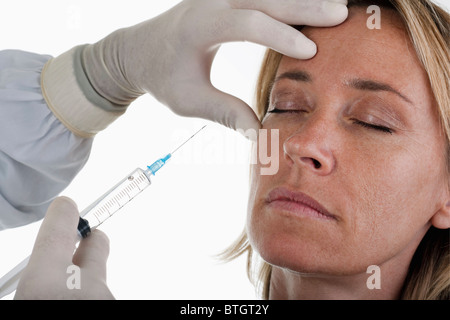 Mano che tiene il botox siringa al volto di donna Foto Stock