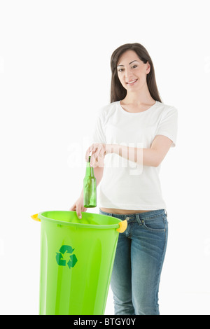 Giovane donna di gettare una bottiglia di vetro nel contenitore di riciclaggio Foto Stock
