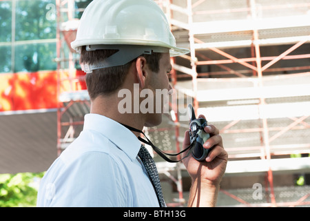 Uomo con casco e walky talky radio al sito in costruzione Foto Stock