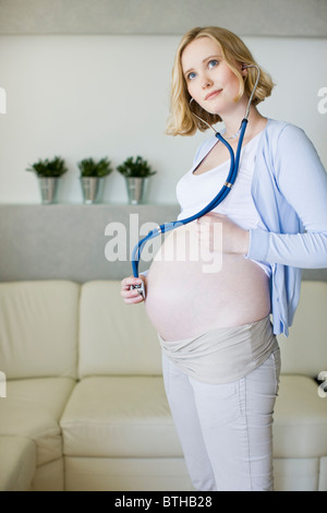 Donna incinta tenendo lo stetoscopio sulla pancia Foto Stock