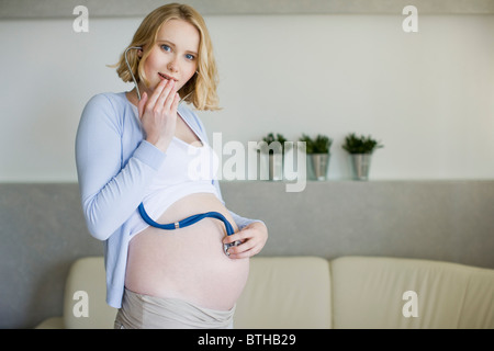 Donna incinta tenendo lo stetoscopio sulla pancia Foto Stock