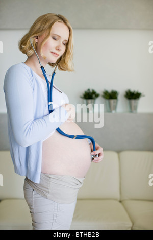 Donna incinta tenendo lo stetoscopio sulla pancia Foto Stock