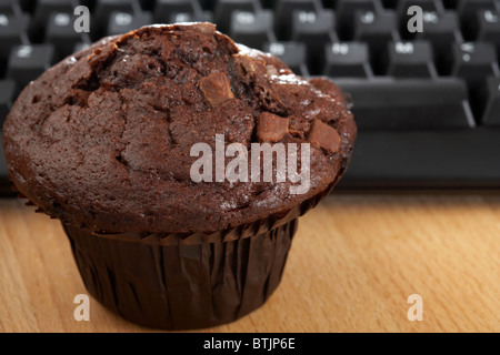 Doppio chip di choc muffin al cioccolato nella parte anteriore della tastiera del computer a pranzo Foto Stock