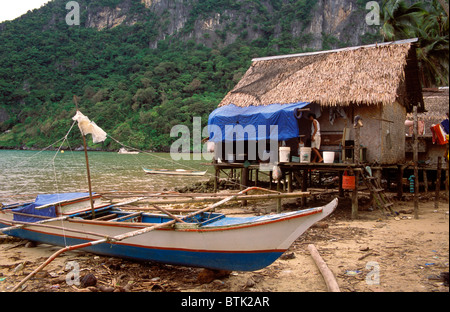 Filippine, Palawan pescatori della barca, volgare bamboo hut e scogliere carsiche di foresta in un villaggio di pescatori a El Nido. Foto Stock