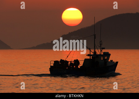 Sunrise over Jethou come un altro peschereccio si allontana Foto Stock