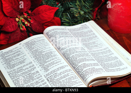 La Bibbia aperta a la storia della natività in Luca con poinsettia, evergreen, e candela Foto Stock