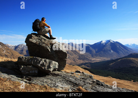 Hillwalker poggiante su una roccia e guardando attraverso Glen Etive a Ben Starav. Foto Stock