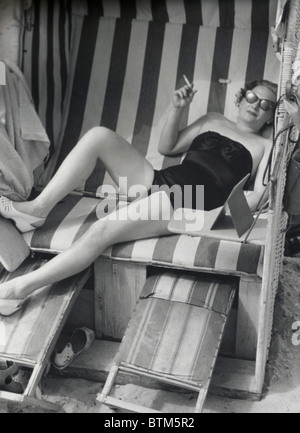 Foto storiche (1910) di una donna seduta su una sedia di spiaggia Foto Stock