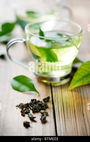 Primo piano di estratto secco di tè verde e una tazza con Freschi Tè verde. in background, al di fuori della messa a fuoco con la tazza di tè freschi Foto Stock