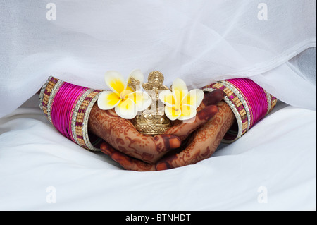 Ragazza indiana indossando di seta bianca sari con henné mani tenendo un fiore di frangipani e una statua di Ganesha. India Foto Stock