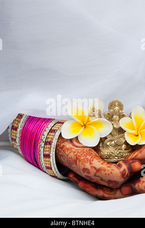 Ragazza indiana indossando di seta bianca sari con henné mani tenendo un fiore di frangipani e una statua di Ganesha. India Foto Stock