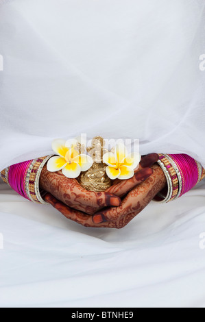 Ragazza indiana indossando di seta bianca sari con henné mani tenendo un fiore di frangipani e una statua di Ganesha. India Foto Stock