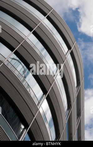 Vista della curva esterna edificio per uffici a guardare in alto verso il blu e il cielo nuvoloso Foto Stock