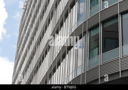Vista della curva esterna edificio per uffici a guardare in alto verso il blu e il cielo nuvoloso Foto Stock