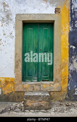 Verde porta di legno con la mano la pietra scolpita contro una parete testurizzata nel borgo medievale di Obidos Foto Stock