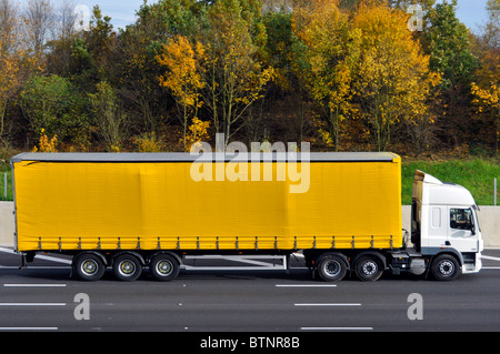 Vista laterale lunga gialla tenda morbida pulita senza contrassegno rimorchio articolato facile accesso cabina autocarro hgv bianca e conducente che viaggia su autostrada M25 Regno Unito Foto Stock
