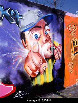 Graffiti di un uomo con un tappo di fondo rivolta verso il suo dito indice all'osservatore / visualizzatore durante la soffiatura in un fischio, Delft Foto Stock