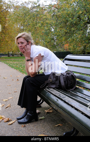 Ritratto di una donna con il mento appoggiato sulle mani & seduto da solo su una panchina nel parco Foto Stock