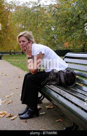 Ritratto di una donna con il mento appoggiato sulle mani & seduto da solo su una panchina nel parco Foto Stock