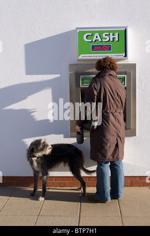 Donna con cane rendendo prelievo contanti da ATM Foto Stock