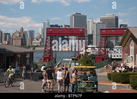 Un traghetto che arrivano e visitatori vicino Governors Island Soissons Dock, dello skyline di Manhattan e Staten Island Ferry a distanza Foto Stock