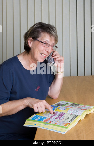 Signora utilizzando elenco telefonico al telefono per i servizi. Foto Stock