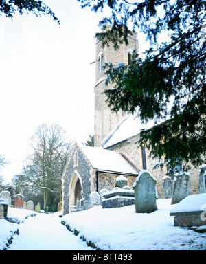 Una scena invernale in un sagrato di Norfolk con una coperta di neve il percorso che conduce alla chiesa. Foto Stock