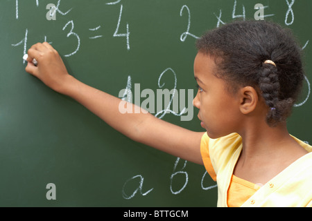 Ritratto di smart schoolchild in piedi alla lavagna e facendo le somme Foto Stock