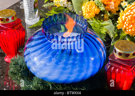 Candele accese e fiori su una lastra tombale Foto Stock