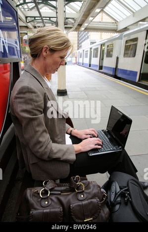 Imprenditrice utilizzando un computer netbook seduto su una stazione ferroviaria platform Foto Stock