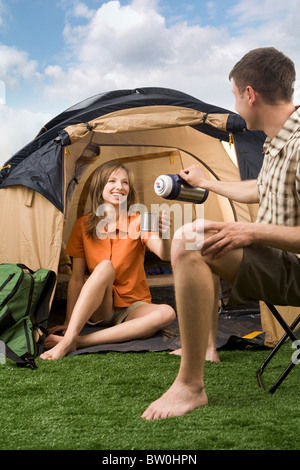 Foto della ragazza allegra coppa di ritegno mentre il suo fidanzato versando il tè in esso nel parco Foto Stock