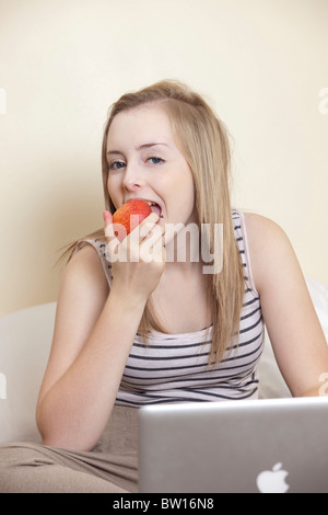 Una ragazza adolescente mangia un Apple mentre studiano nella sua camera da letto REGNO UNITO Foto Stock