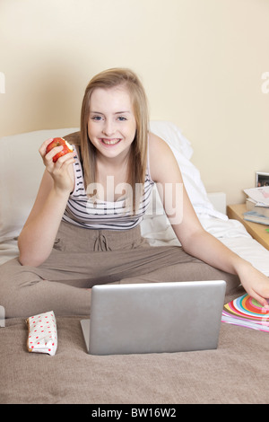 Una ragazza adolescente mangia un Apple mentre studiano nella sua camera da letto REGNO UNITO Foto Stock