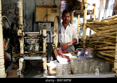 Uomo in piedi accanto alla macchina a spremere il succo di canna da zucchero e in India; macchina spreme il succo dalla canna da zucchero per fare bevande fresche Foto Stock