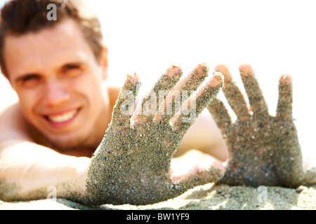 Foto di sorridere ragazzo disteso sulla spiaggia e mostra le sue mani ricoperte di sabbia mentre si prende il sole Foto Stock