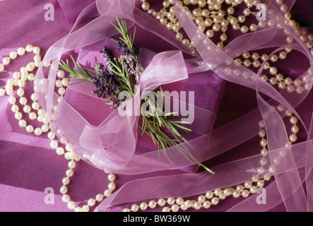 Still-Life della stringa di faux-perle e regalo di compleanno avvolti con carta viola e legato con erbe fresche e malva ribbon Foto Stock