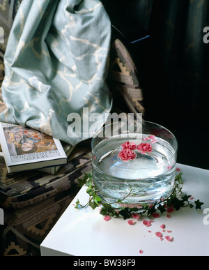 Still-Life di petali di rosa galleggianti in acqua nel vaso di vetro sul tavolo contro i tessuti in blu pallido Foto Stock