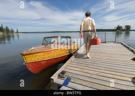 Uomo che cammina con gas può verso il Mogano barca a motore Lago Gunn, Ontario Foto Stock