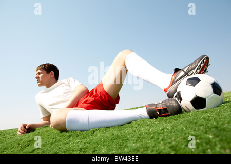Foto di pensieroso il calciatore giacente su erba verde-campo e di appoggio Foto Stock