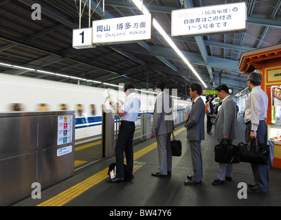 Azienda giapponese uomini fodera fino a immettere un Shinkansen treno arrivando alla piattaforma di Shin Kobe, Hyogo, Giappone JP Foto Stock