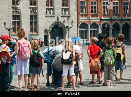 Markt, Bruges, Belgio, Europa. Gruppo di bambini indossare zaini su una gita scolastica a la storica piazza della città Foto Stock