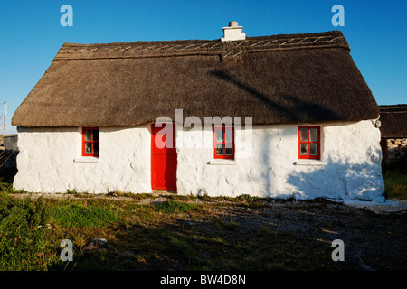 Cottage con il tetto di paglia con porta rossa, vicino Rossaveel, Connemara, nella contea di Galway, Connaught, Irlanda. Foto Stock