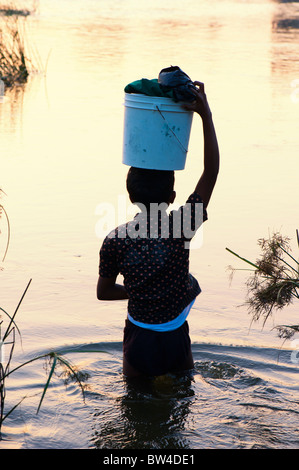 Silhouette di un ragazzo che trasportano il lavaggio in una benna sulla sua testa in un fiume in India a sunrise. Puttaparthi, Andhra Pradesh, India Foto Stock